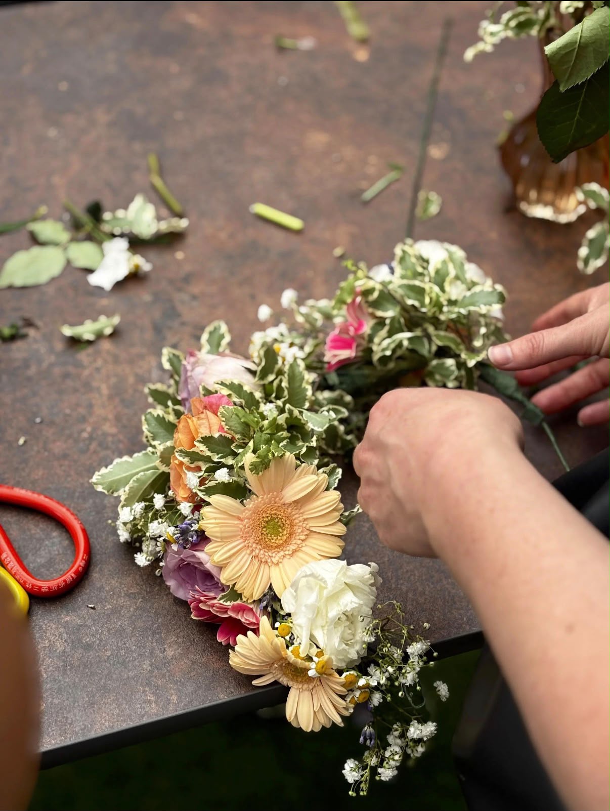 Hands weaving a natural flower crown with soft pastel blooms
